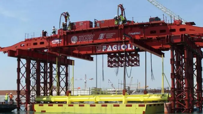 Una immagine dell'installazione della prima paratoia del Mose, Venezia, 14 giugno 2013. Posizionata ieri nel canale di Lido-Treporti, sono iniziate le operazioni di varo: la paratoia è stata lentamente calata in acqua per essere installata nel "cassone" di alloggiamento sott'acqua tramite uno speciale "mezzo di varo". ANSA / US CONSORZIO VENEZIA NUOVA ++NO SALES EDITORIAL USE ONLY++