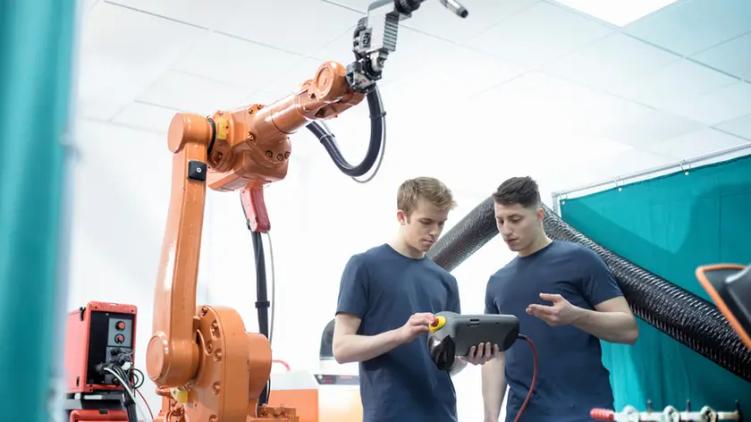 Two male engineers controlling robotic welder in factory.