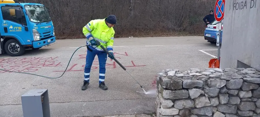 Gli operatori al lavoro per rimuovere le scritte all'ingresso della Foiba (foto Massimo Silvano)