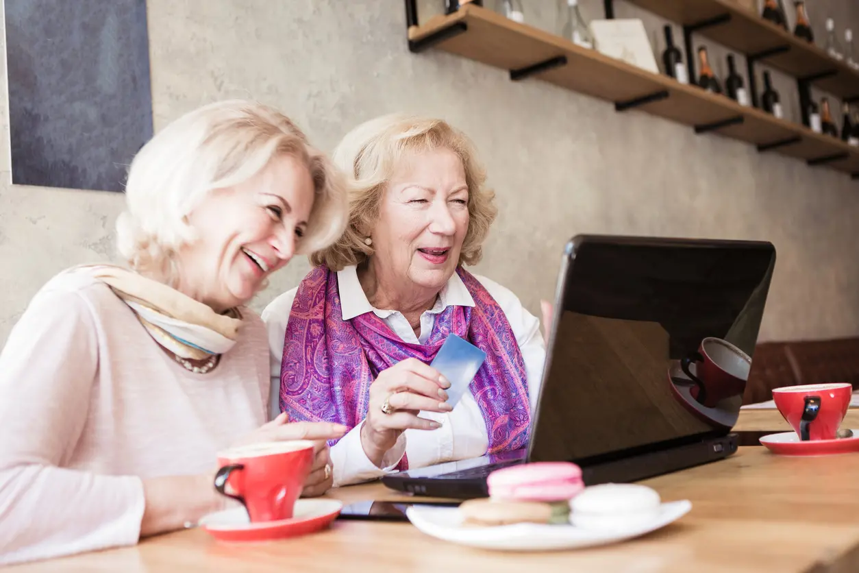 Two senior women, using laptop in caffe, shopping online, paying with card
