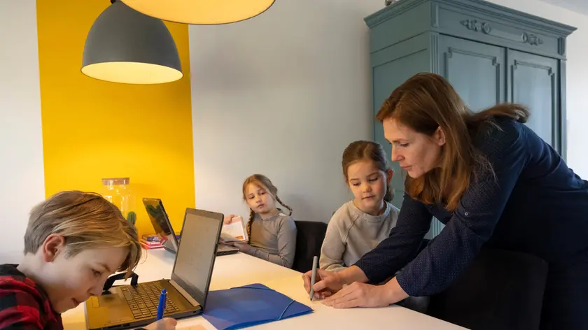 Family indoors during Corona virus crisis, mother and three children sitting at table with laptop computer, doing homework.