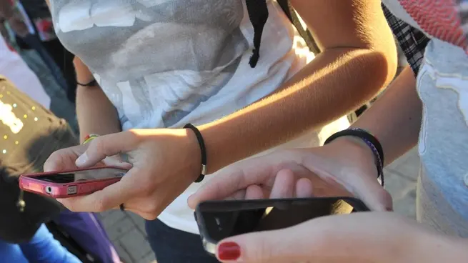 Due ragazze si scambiano messaggi sugli iPhone prima di entrare a scuola.ANSA/FRANCO SILVI