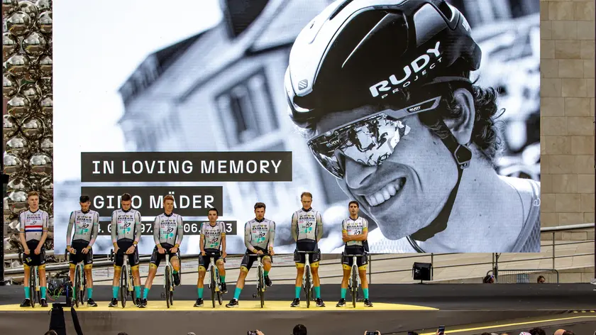 epa10718052 Cyclists of Bahrain Victorious team observe a minute of silence for their late teammate, Swiss rider Gino Mader (pictured on screen), during the team presentation of the Tour de France 2023 in Bilbao, Spain, 29 June 2023. The Tour de France 2023 will start in Bilbao on 01 July. EPA/MARTIN DIVISEK