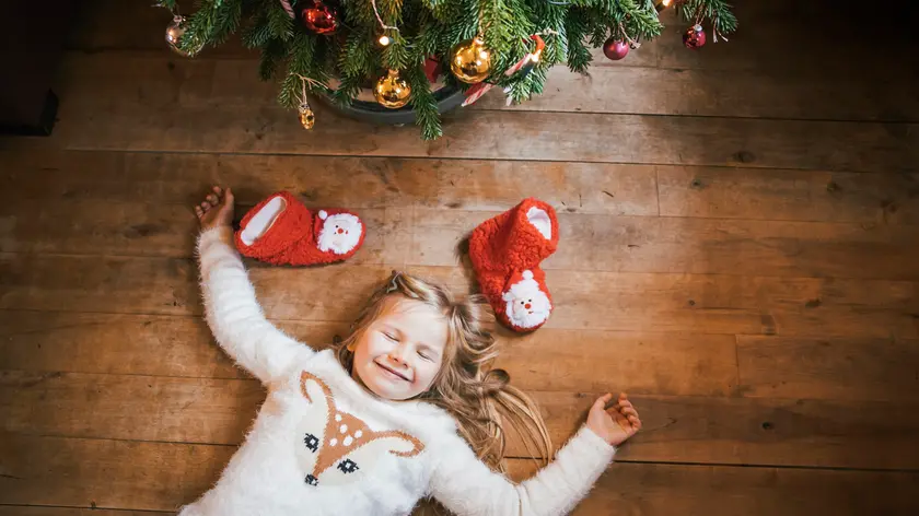 Smiling girl with closed eyes lying under the Christmas tree