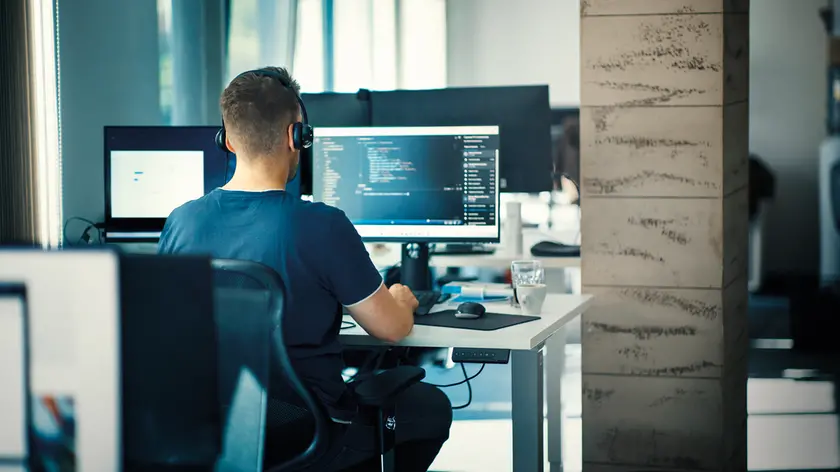 Closeup rear view of a young man coding on multiple computers