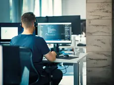 Closeup rear view of a young man coding on multiple computers