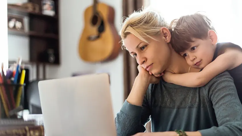 A cute little boy hugging his mom tightly while she is working.