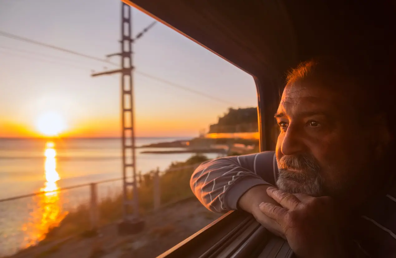 Elderly man admires sunset over the sea from open window of train
