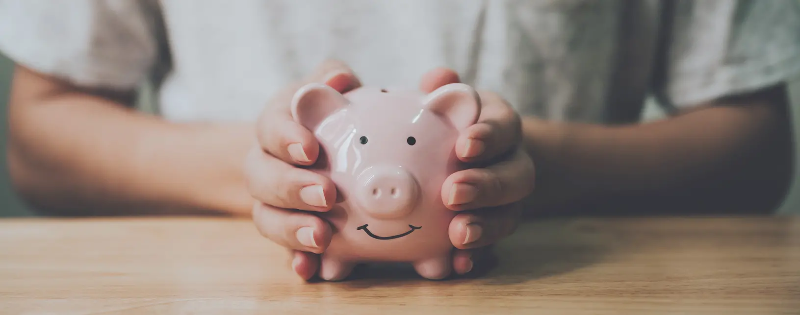 Panoramic image, Man hand holding piggy bank on wood table. Save money and financial investment