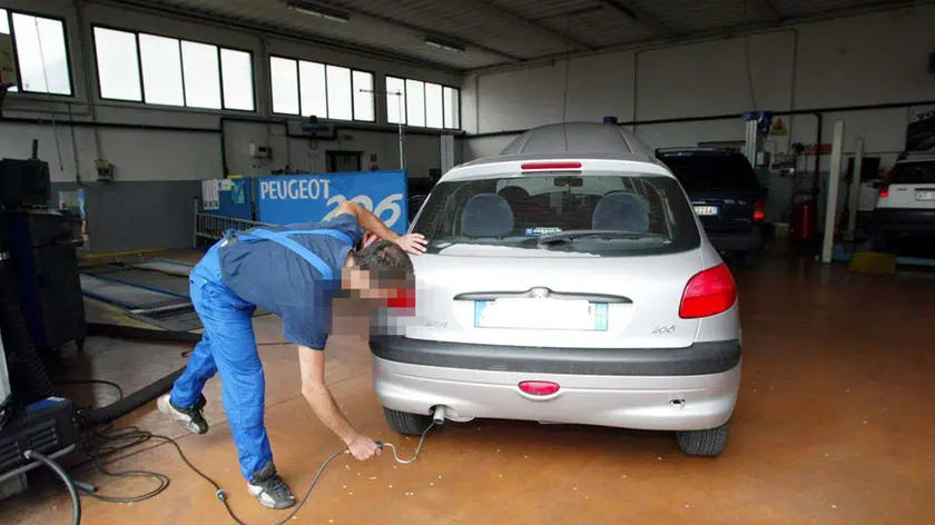 MECCANICO CONTROLLA EMISSIONE DEI GAS DI SCARICO DI UN'AUTO PER IL RILASCIO DEL BOLLINO BLU IN UNA AUTOFFICIANA CENTRO REVISIONI CENTRO REVISIONE