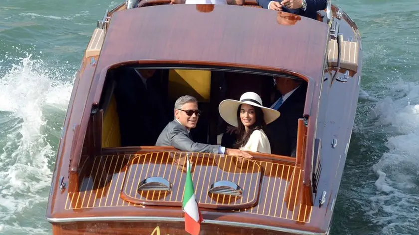 George Clooney, flanked by his wife Amal Alamuddin, sit on a water-taxi after leaving the city hall in Venice, Italy, Monday, Sept. 29, 2014. George Clooney married human rights lawyer Amal Alamuddin Saturday, the actor's representative said, out of sight of pursuing paparazzi and adoring crowds. (AP Photo/Luigi Costantini)