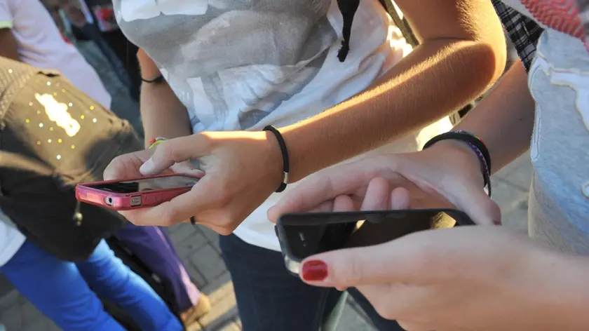 Due ragazze si scambiano messaggi sugli iPhone prima di entrare a scuola.ANSA/FRANCO SILVI