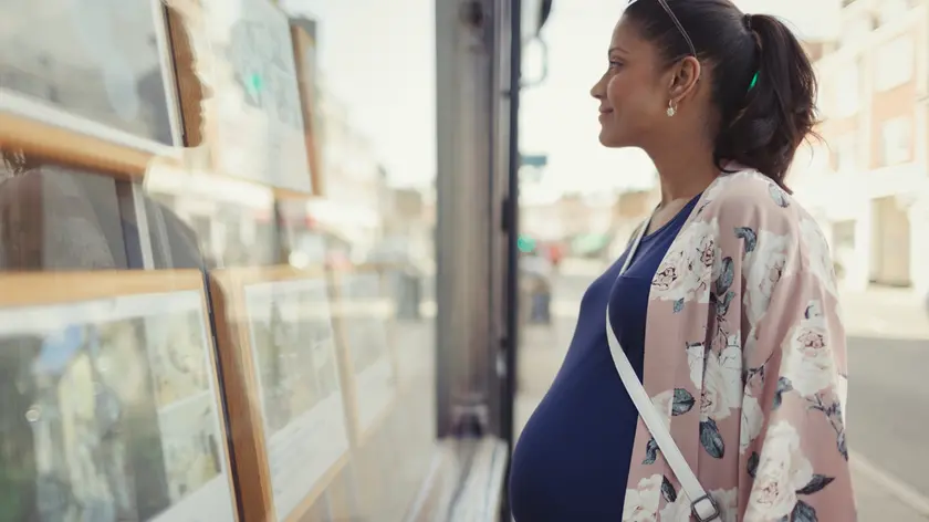 Pregnant woman browsing real estate listings at urban storefront