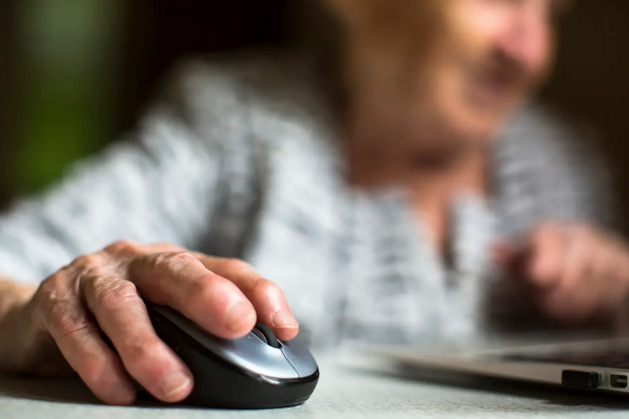Closeup of the hand of an old woman holding a computer mouse.