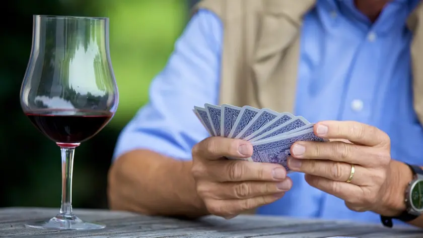 Senior man playing cards and drinking red wine, close_up