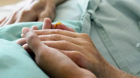 A young hand touches and holds an old wrinkled hand in hospital