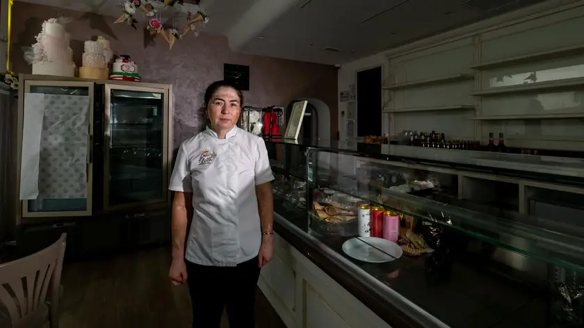 Stella Scutelnic all’interno della sua pasticceria “Dolce Stella” di Casalserugo. Non aveva pagato le bollette, le è stata tolta l’elettricità. A destra la pasticciera con il cartello contro il governo (ZANGIROLAMI)